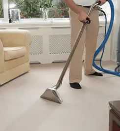 Professional carpet cleaner using a hot-water extraction wand and hose machine in a living room in Seattle, WA.