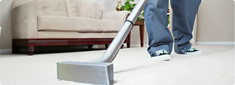 Carpet cleaning technician using a hot-water extraction wand on a light-colored carpet in a living room, Seattle, WA.