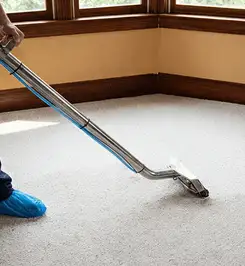Steam carpet cleaning technician using a hot-water extraction wand on a residential carpet, wearing blue protective shoe covers Seattle, WA.